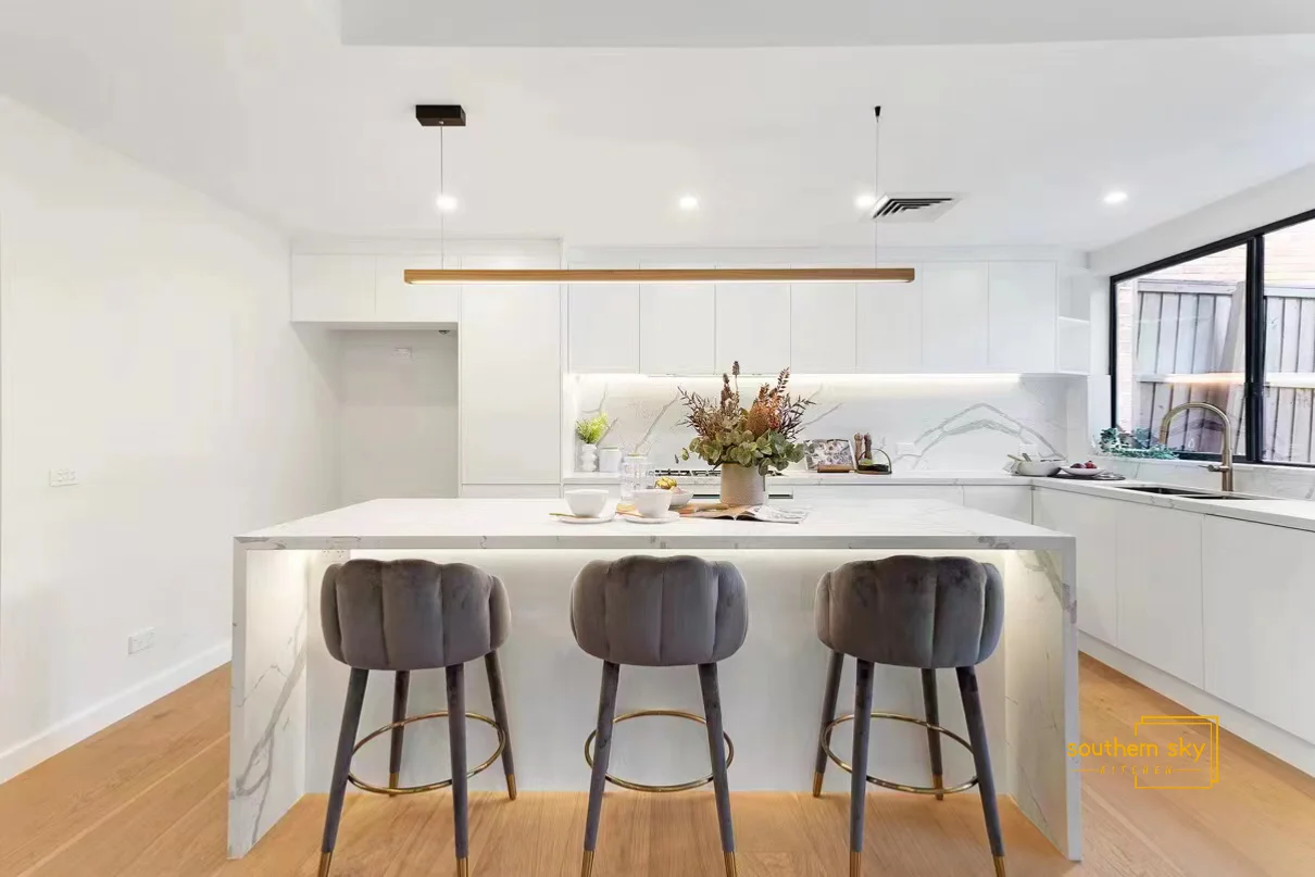 Elegant kitchen with minimalist design, marble island, plush bar stools, and sleek lighting for a modern, luxurious feel.
